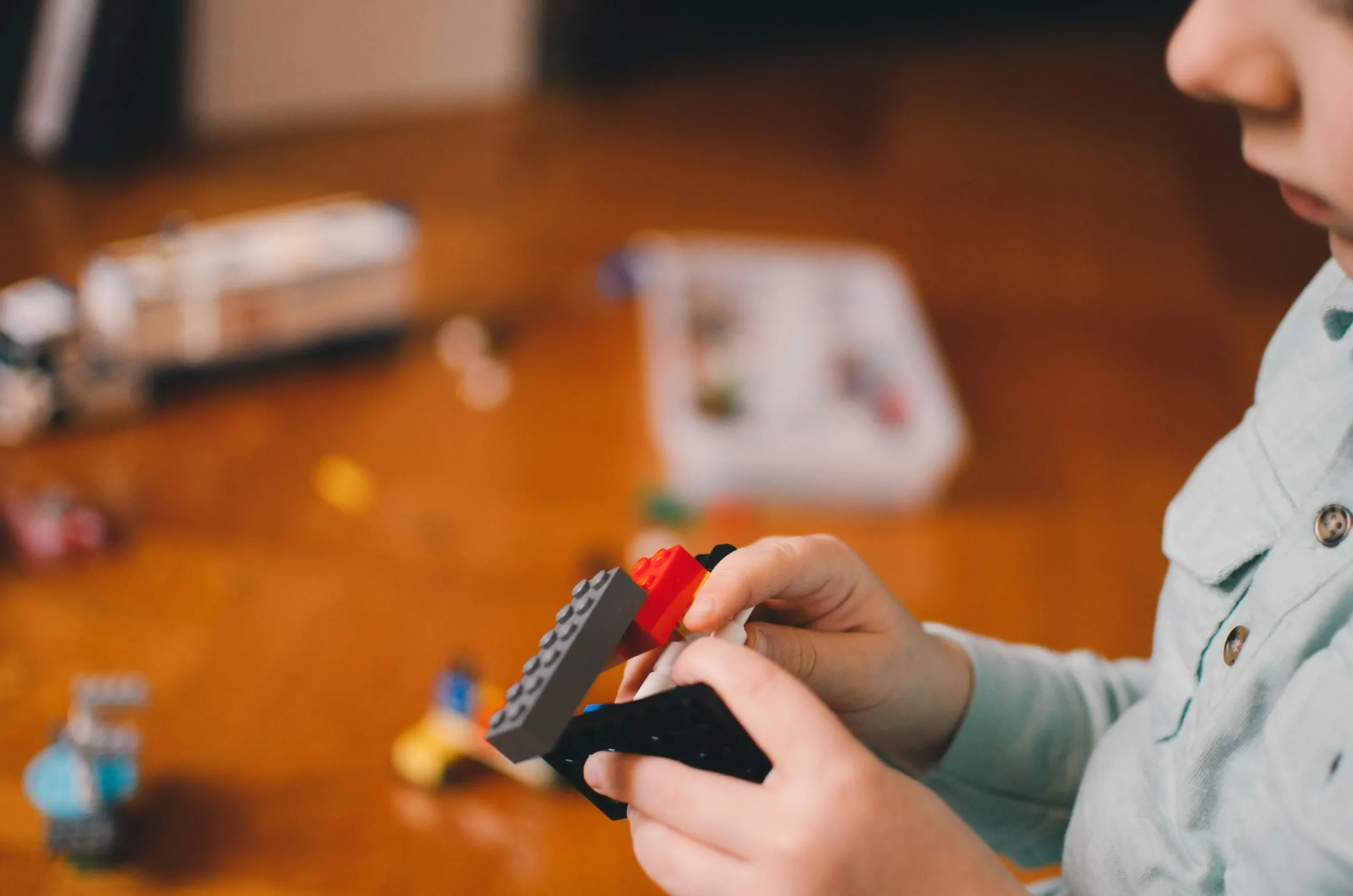 Close-up of a child connecting grey, red, and black building blocks.